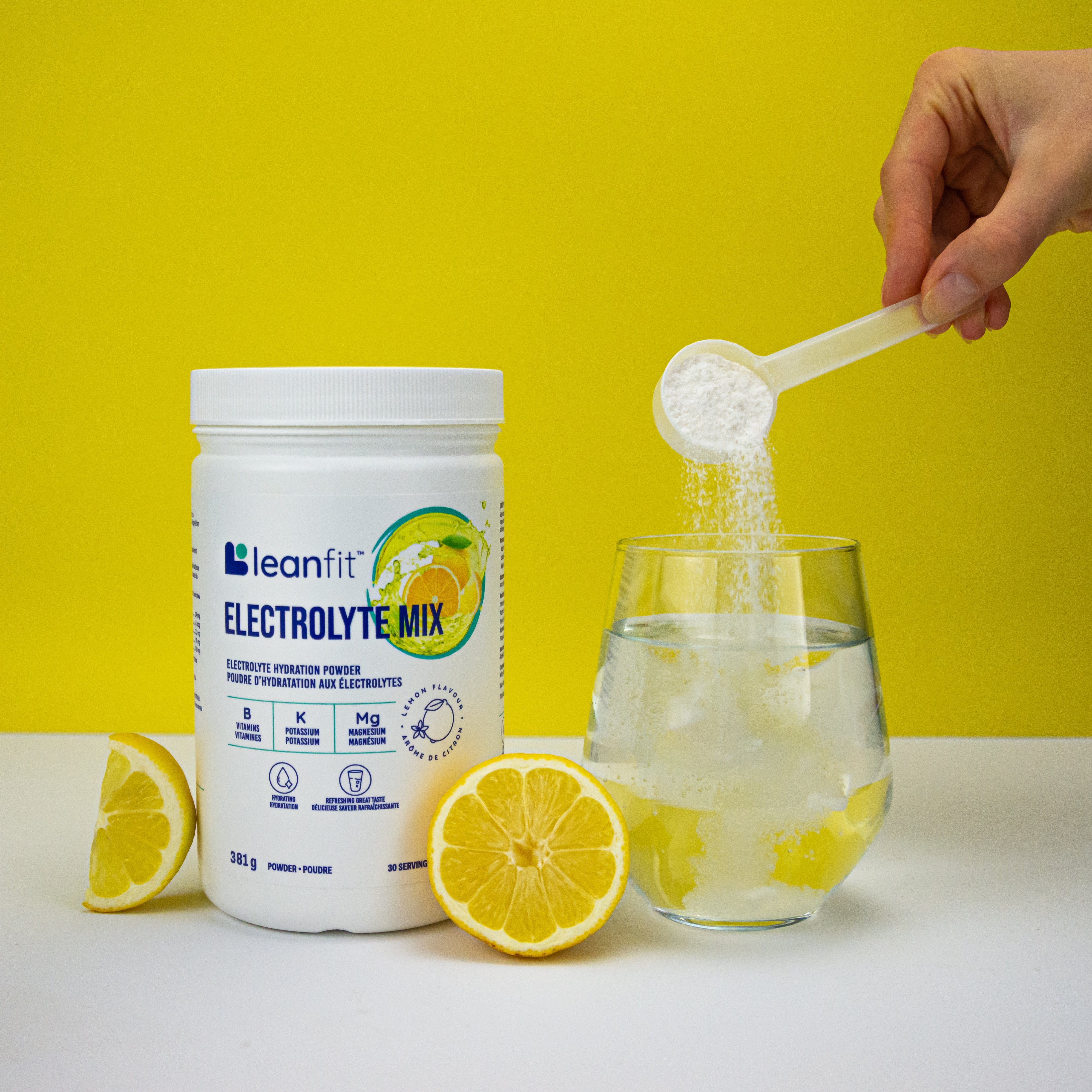 Scooping LEANFIT Electrolyte Mix into a glass with lemon — easy to mix and enjoy