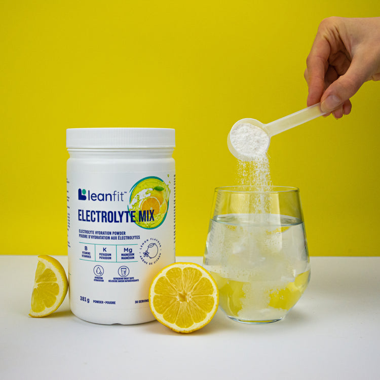 Scooping LEANFIT Electrolyte Mix into a glass with lemon — easy to mix and enjoy