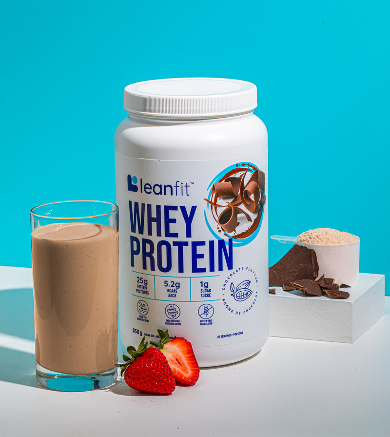 Leanfit whey protein container with a glass of chocolate protein shake, strawberries, and chocolate pieces on a blue background.